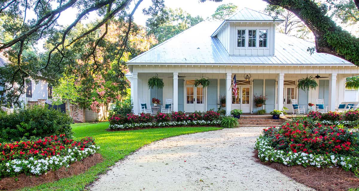Home with curved driveaway and large oak tree and plantings of Encore Azalea flowers in red and white